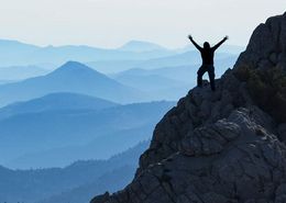 Ein Mensch freut sich über den Aufstieg auf einen Berg.