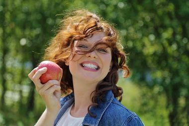 Elinde bir elma tutan kadın kameraya gülümsüyor.