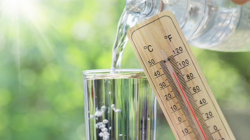 In ein Glas wird Wasser eingeschüttet und ein Thermometer zeigt 38 Grad an.
