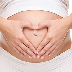 Schwangere Frau hält sich Hände in Herzform über den Bauch.