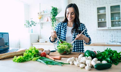 Bir kadın bir mutfakta salata hazırlıyor.