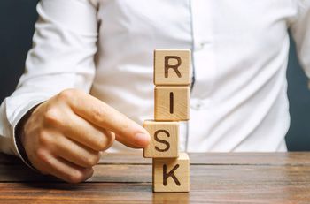 A man is removing a wooden dice from a tower of wooden dice spelling out the word “risk”.