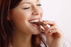 A young woman biting into a piece of chocolate from a bar.