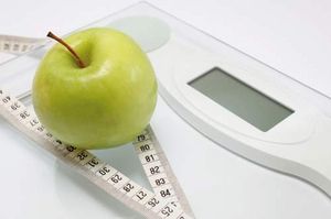 An apple and a measuring tape on a pair of scales.