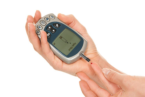 Ein Blutglukosemessgerät wird mit der einen Hand an den Blutstropfen an einem Finger der anderen Hand gehalten.