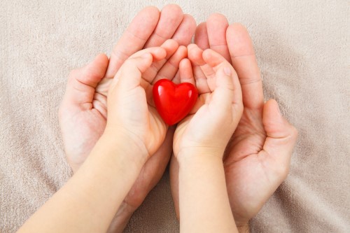 Kinderhand hält Herz und liegt in Erwachsenenhand