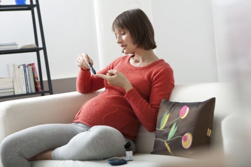 schwangere Frau sitzt auf Sofa und misst Blutzucker