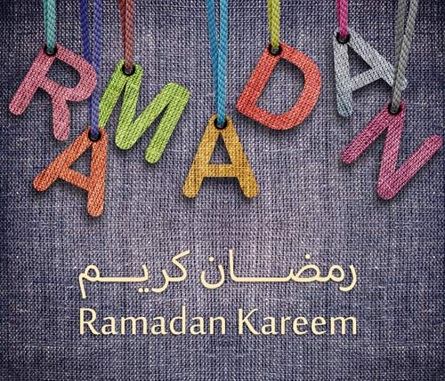 Colorful letters made of fabric hang on threads. The letters form the word "Ramadan". Below, "Ramadan Kareem" is written in Latin and Arabic script.