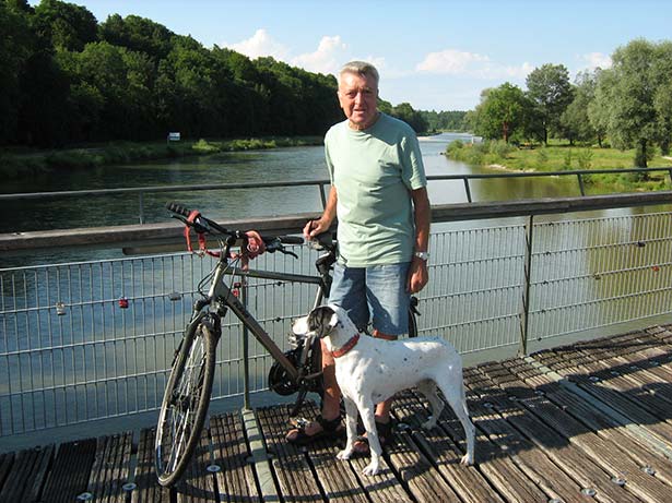 Johann G. steht im Sommer mit seinem Fahrrad und seinem Hund auf einer Brücke