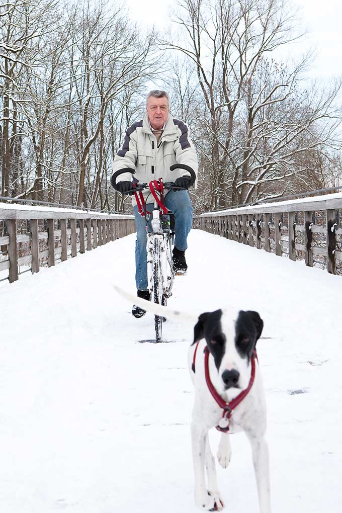 Johann G. fährt Fahrrad im Winter, sein Hund läuft an der Seite mit