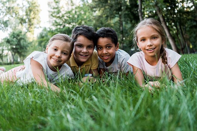 4 Kinder liegen lachend im Gras auf einer Wiese