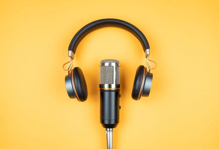 Ein Mikrofon und Kopfhörer liegen auf einem gelben Untergrund.