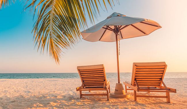 An einem Strand stehen 2 Liegestühle und ein Sonnenschirm.