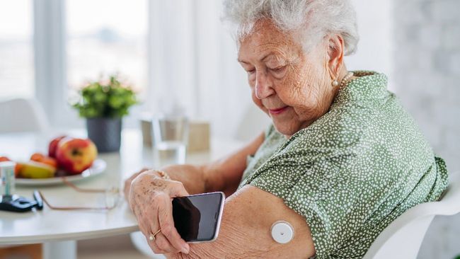Ältere Frau mit Sensor am Arm misst Blutzucker.