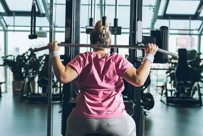Rückenansicht einer Frau, die in einem Fitnesstudio an einem Gerät trainiert.