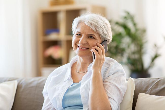 Eine ältere Frau sitzt auf einer Couch und telefoniert mit einem Handy.