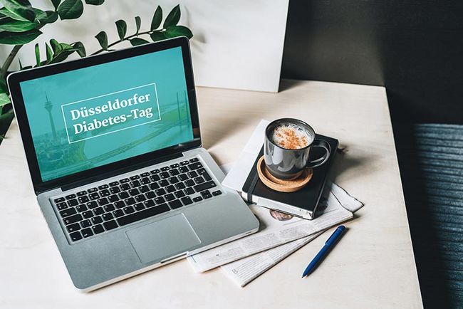 Schreibtisch mit einem aufgeklappten Laptop, Zeitungen und einer Tasse Kaffee.