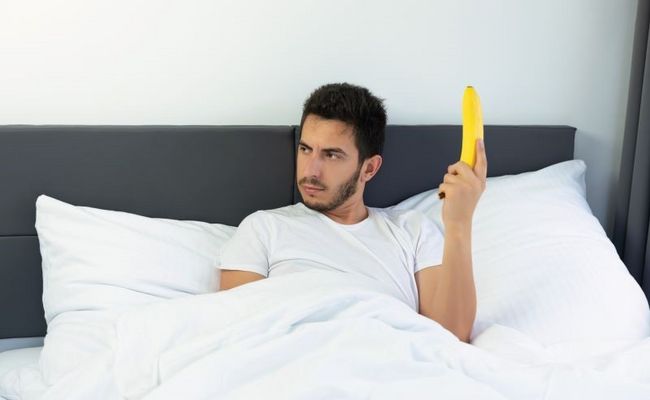 Ein Mann liegt im Bett und hält eine Banane in der Hand