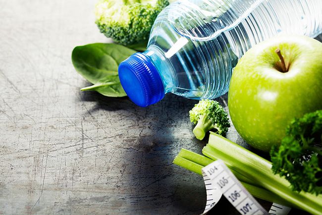 Auf dem Boden liegen eine Wasserflasche, ein Maßband sowie Obst und Gemüse.
