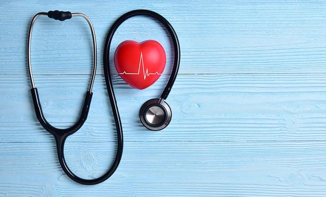 Ein Stethoskop liegt auf einem Tisch zusammen mit einem roten Herz.