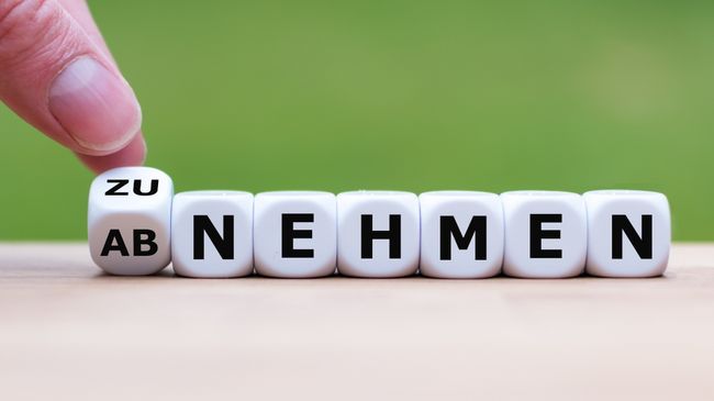 Hand dreht Würfel um mit den Buchstaben 'ZU' und 'AB' vor Würfeln mit den Buchstaben 'NEHMEN' 