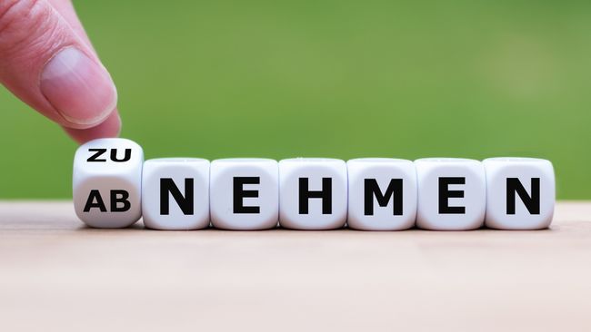 Hand dreht Würfel um mit den Buchstaben 'ZU' und 'AB' vor Würfeln mit den Buchstaben 'NEHMEN' 