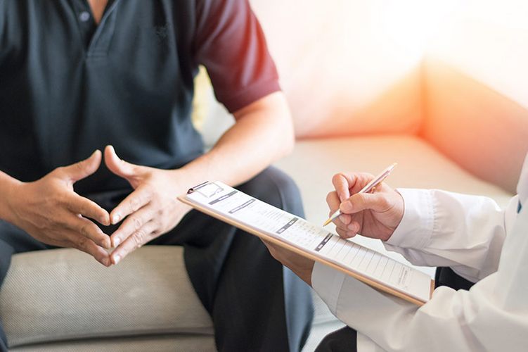 Ein Arzt sitzt mit einer Checkliste in der Hand einem Patienten gegenüber.