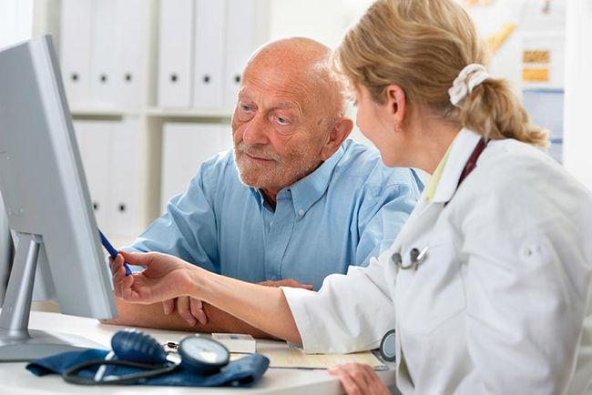 Eine Ärztin zeigt einem älteren Herrn etwas auf einem PC-Bildschirm. 