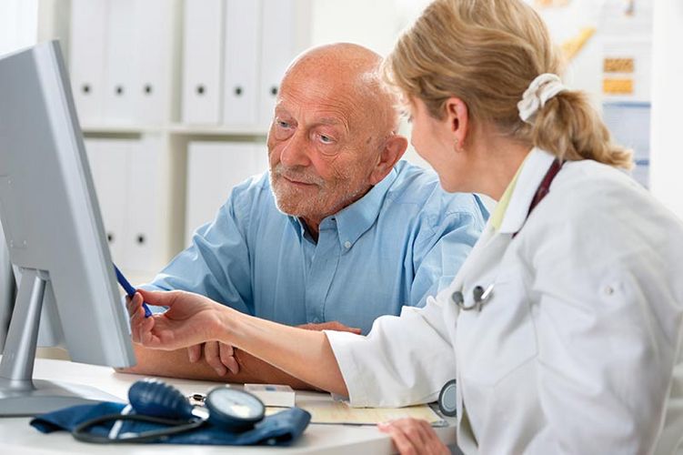 Eine Ärztin zeigt einem älteren Herrn etwas auf einem PC-Bildschirm. 