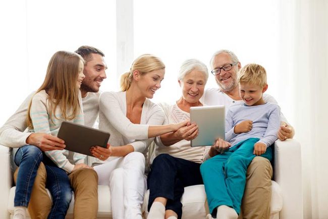 Eine Familie, bestehend aus Eltern, zwei Kindern und den Großeltern, sitzt auf einer Couch und schaut sich etwas auf einem Tablet an.