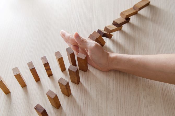 Eine Hand hindert Dominosteine am umfallen