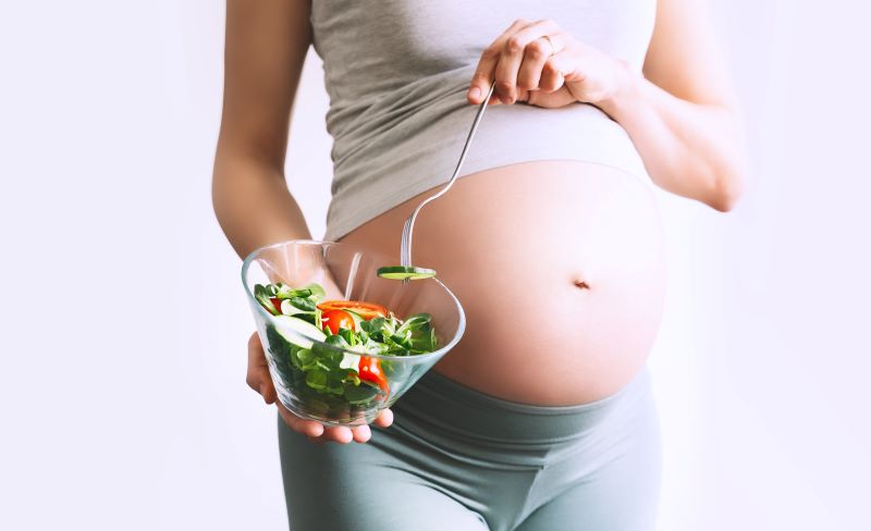 Eine schwangere Frau hält einen Salatteller vor ihren Bauch