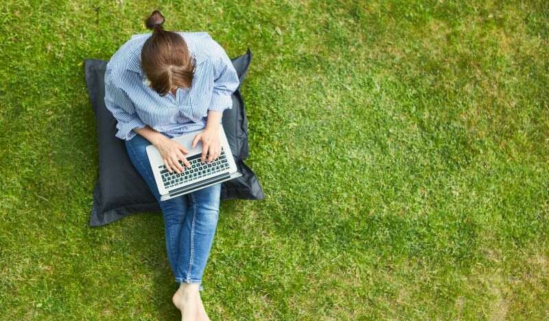 Eine Frau sitzt im Gras mit einem Laptop auf dem Schoß