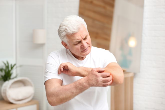 Ein Mann krazt sich am Arm. 