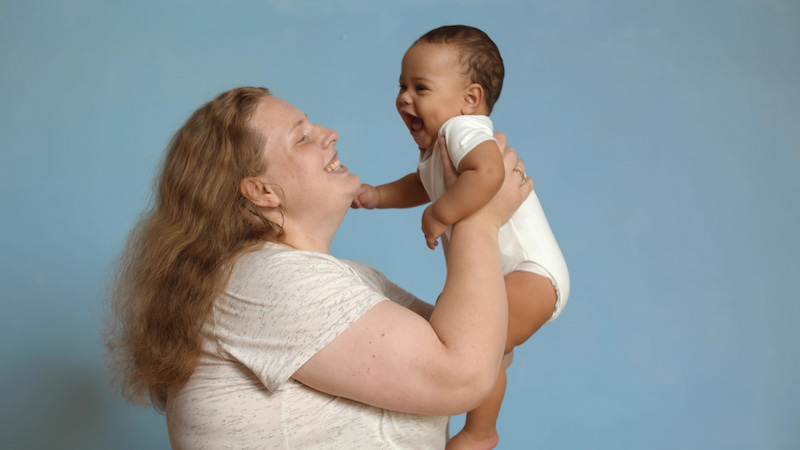 Eine Frau hebt ein Baby in die Luft während beide lächeln